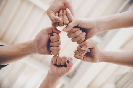 Six hands forming a circle with fists touching in the center.